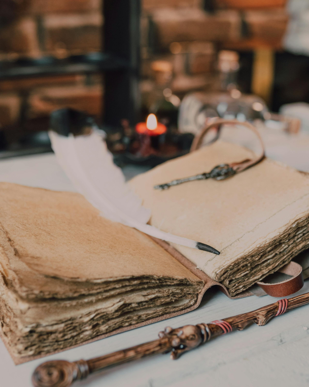 An open, worn book with a feather pen laying over it and a wand laying in front of it.