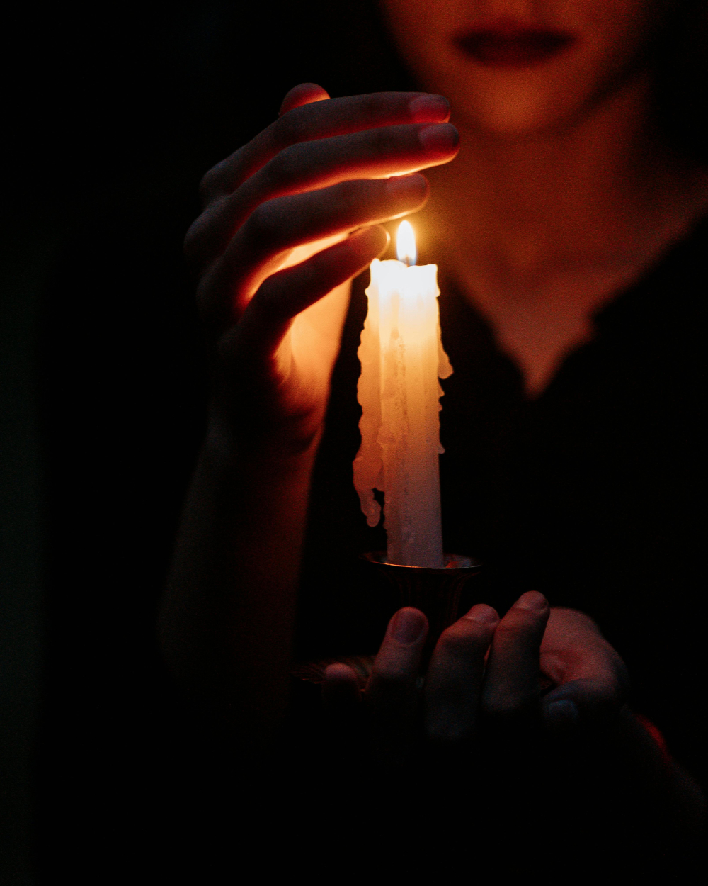 A woman holding a lit candle and shielding it with her hand.